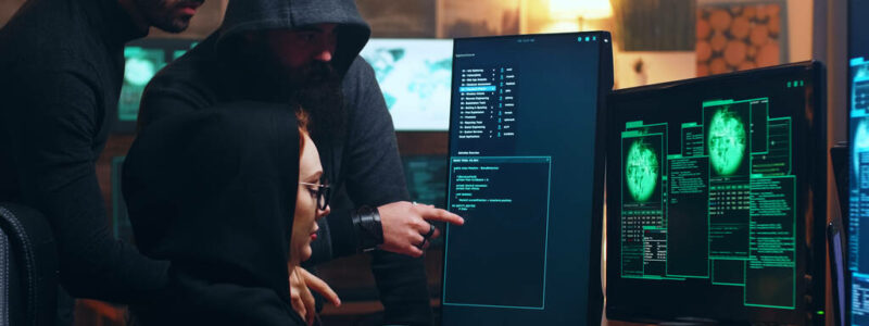 Team of hackers looking at computer with multiple monitors while committing cyber crimes.